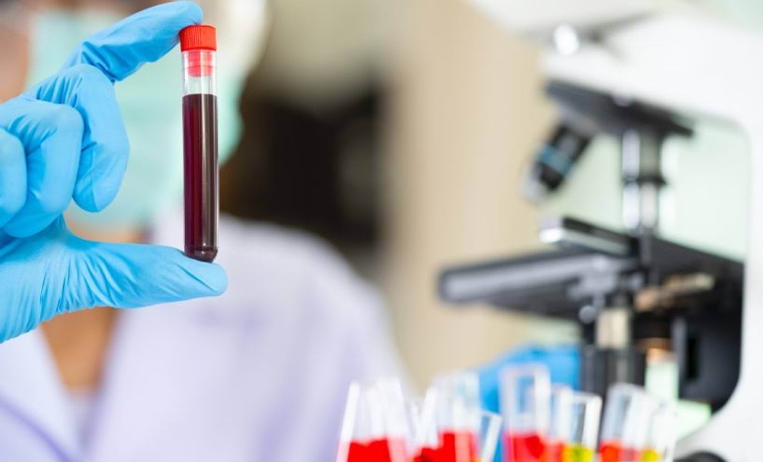 gloved hand holding a tube of blood