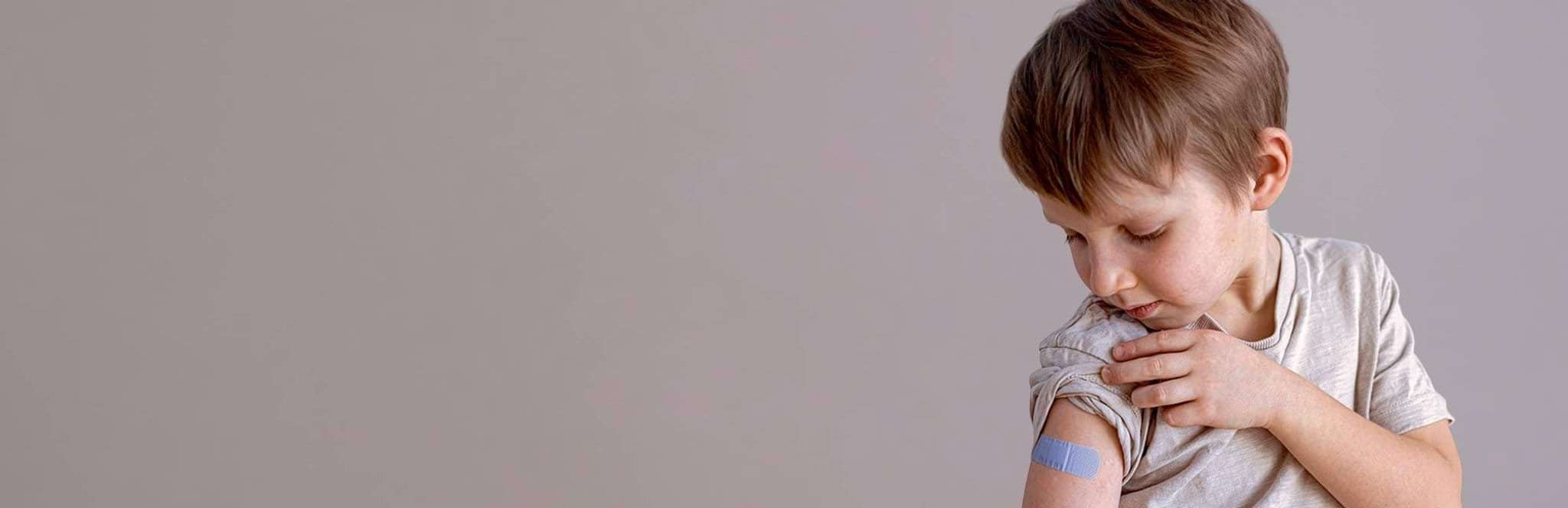 Boy looks at bandaid on arm after vaccination