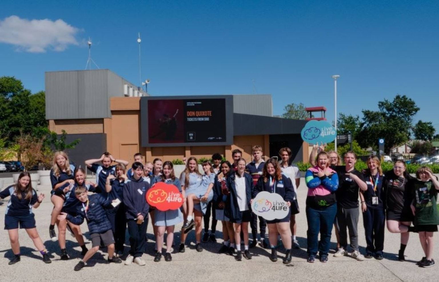 A group of students standing in a group outside, holding signs that represent Live4Life - a mental health organisation.