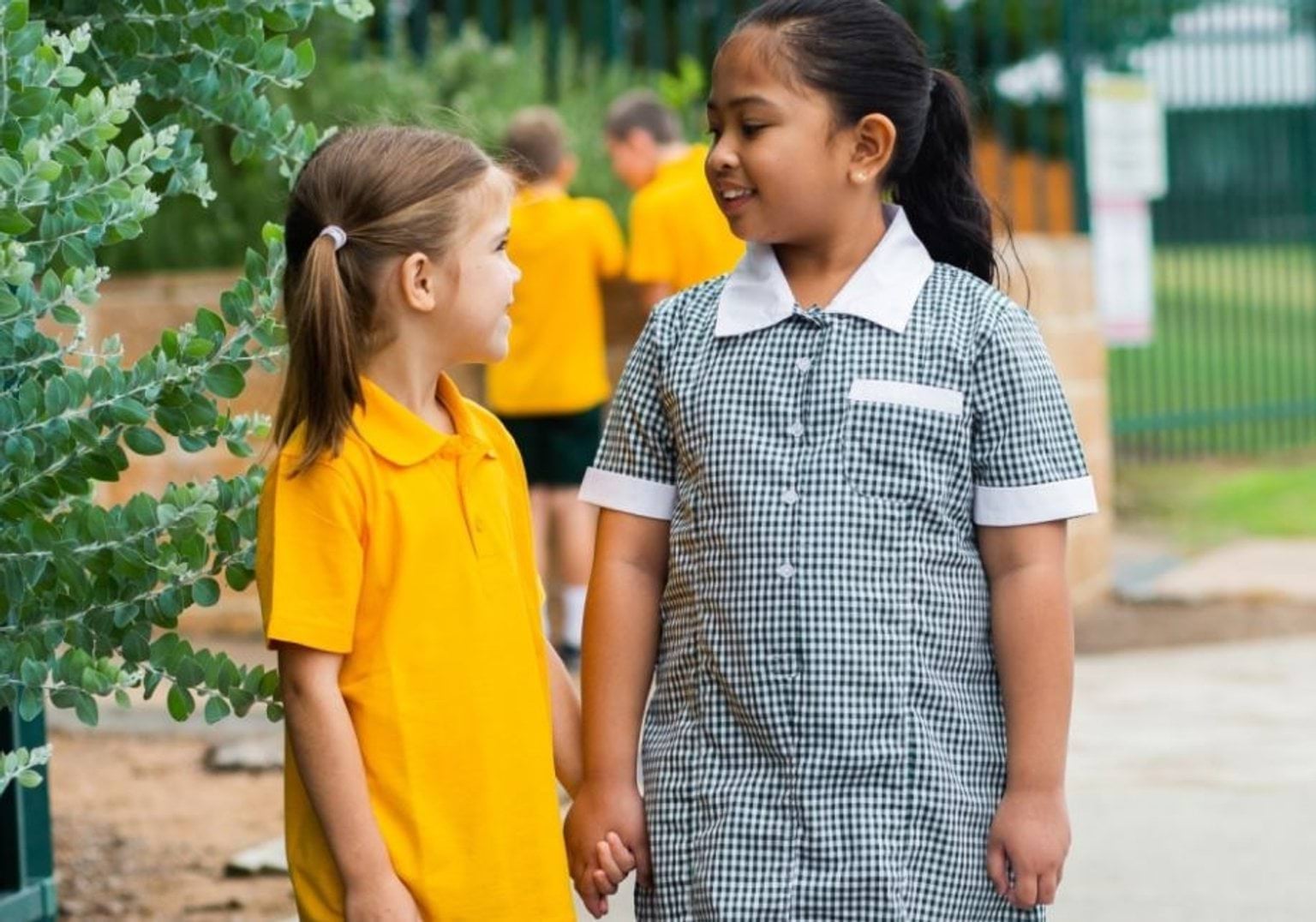 Two young school girls holding hands and smiling at each other.