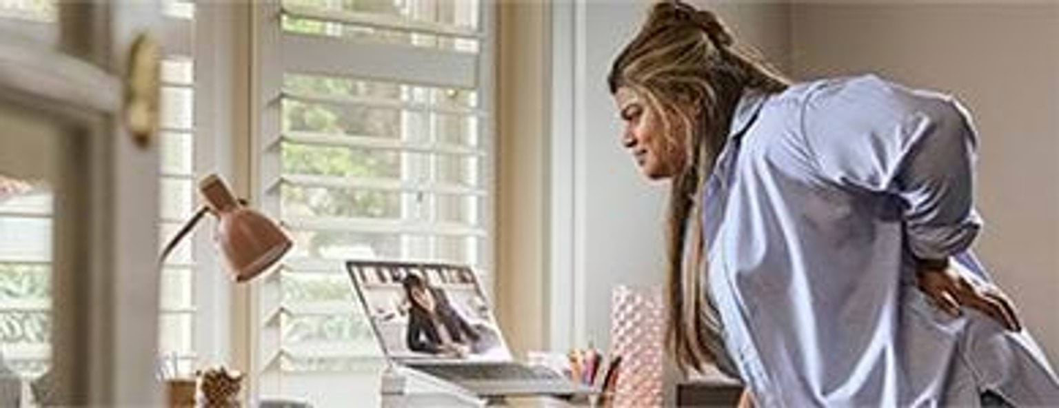 A person holding their strained back on a video call with Virtual Emergency Care, a urgent care service